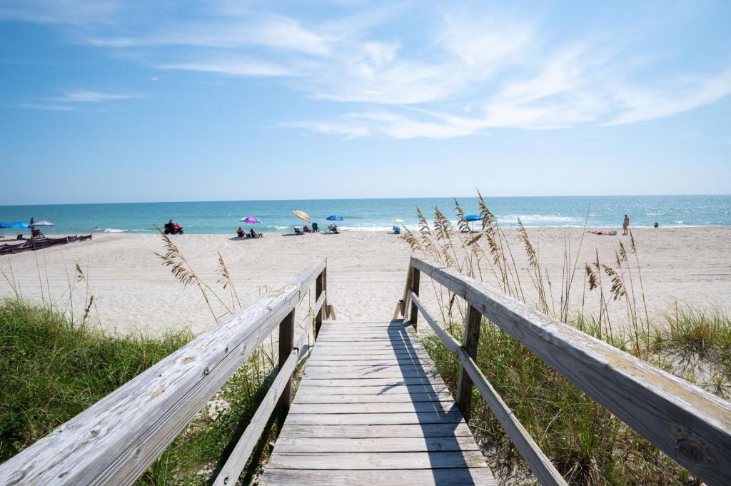 a wooden boardwalk leading to a beach with people at Oceanfront Condo with Pool - Salty Hammocks A6 in Carolina Beach
