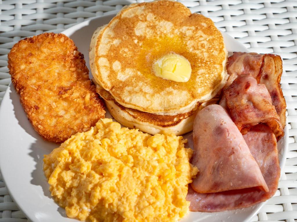 A plated breakfast of pancakes, eggs, bacon, ham and a potato side.