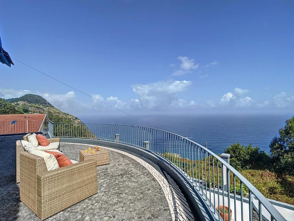 uma cadeira de vime sentada numa varanda com vista para o oceano em Vinhaticos Villa by Atlantic Holiday em Porto Moniz