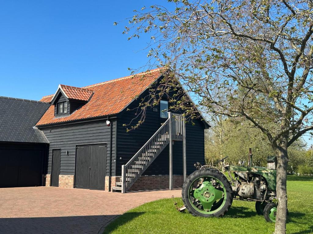 Newbourn的住宿－The Old Piggery, Cart Lodge in Newbourne，前面有拖拉机的黑谷仓