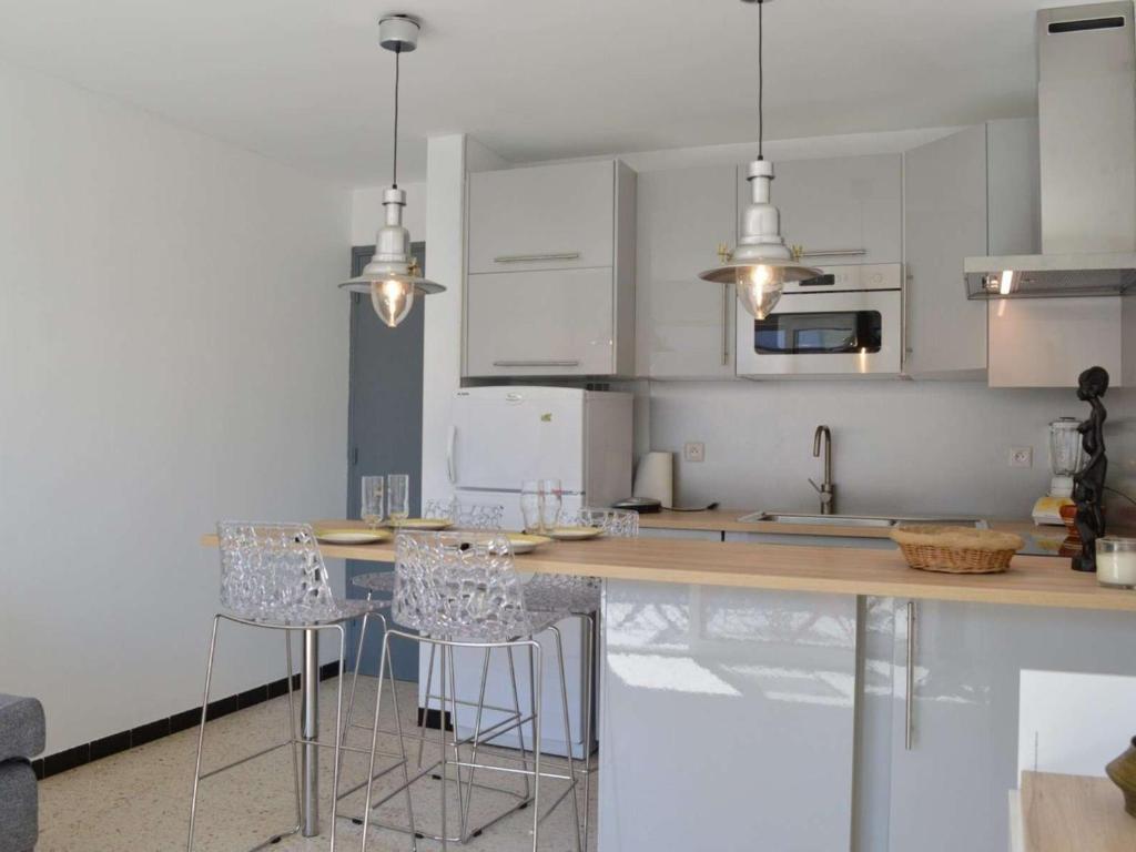 une cuisine avec des armoires blanches et des tabourets de bar dans l'établissement Appartement rénové, climatisé à 200m de la plage avec balcon et parking privé - FR-1-229D-12, à Fleury