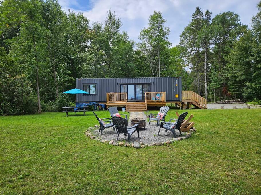 a tiny house in a field with chairs at Stunning Modern Container Home on Golden Lake in Killaloe Station