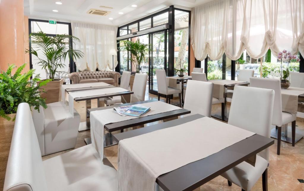 ein Restaurant mit Tischen, weißen Stühlen und Fenstern in der Unterkunft Hotel Novella in Misano Adriatico