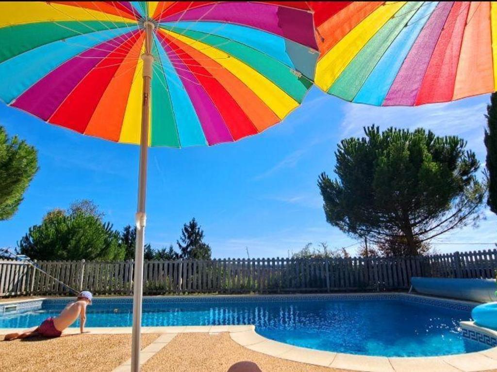 una donna seduta sotto un ombrellone accanto alla piscina di Maison familiale avec piscine privée, jeux pour enfants, salle de sport et Wifi en Dordogne - FR-1-616-70 a Cherveix-Cubas