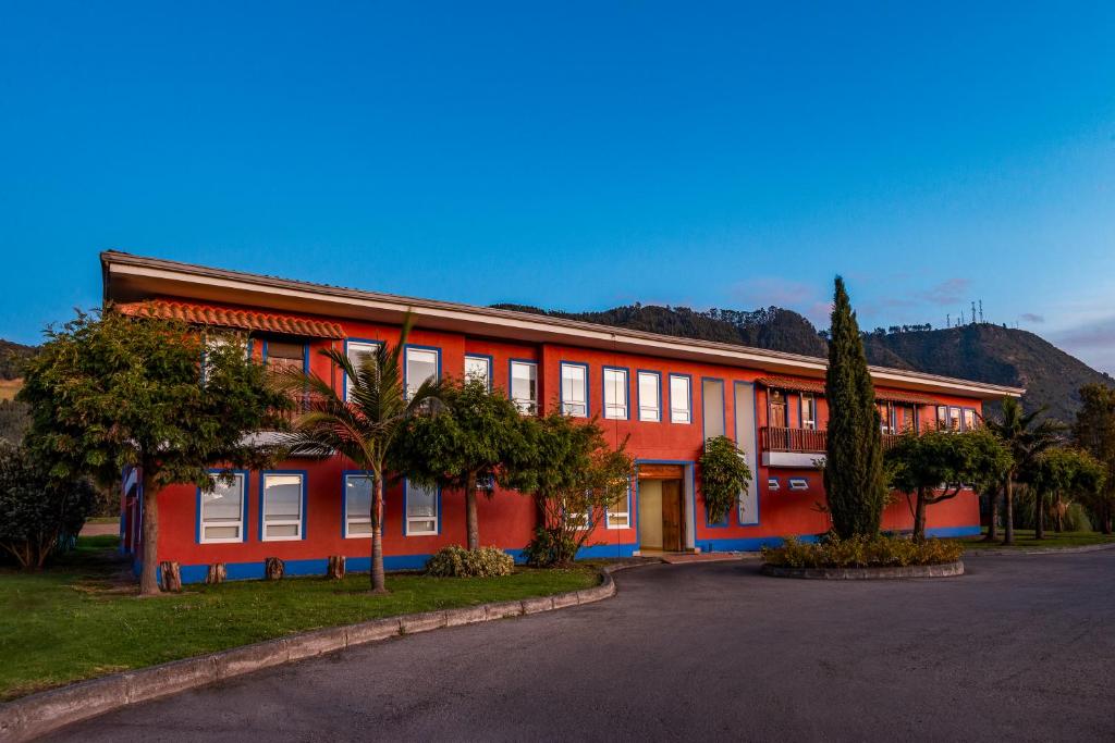 un edificio rosso con alberi di fronte di Hotel Xue Sabana a Cajicá