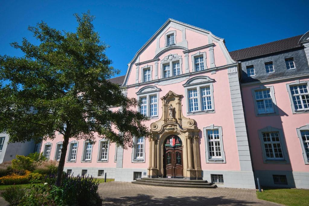 een roze gebouw met een boom ervoor bij Historisches Deluxe Apartment im Marianum in Neuss