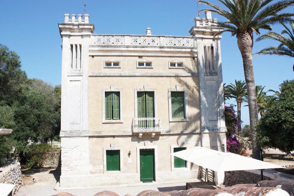 a building with green doors and a palm tree at Sa Cudia Cremada - Palacete en Mahón in Mahón