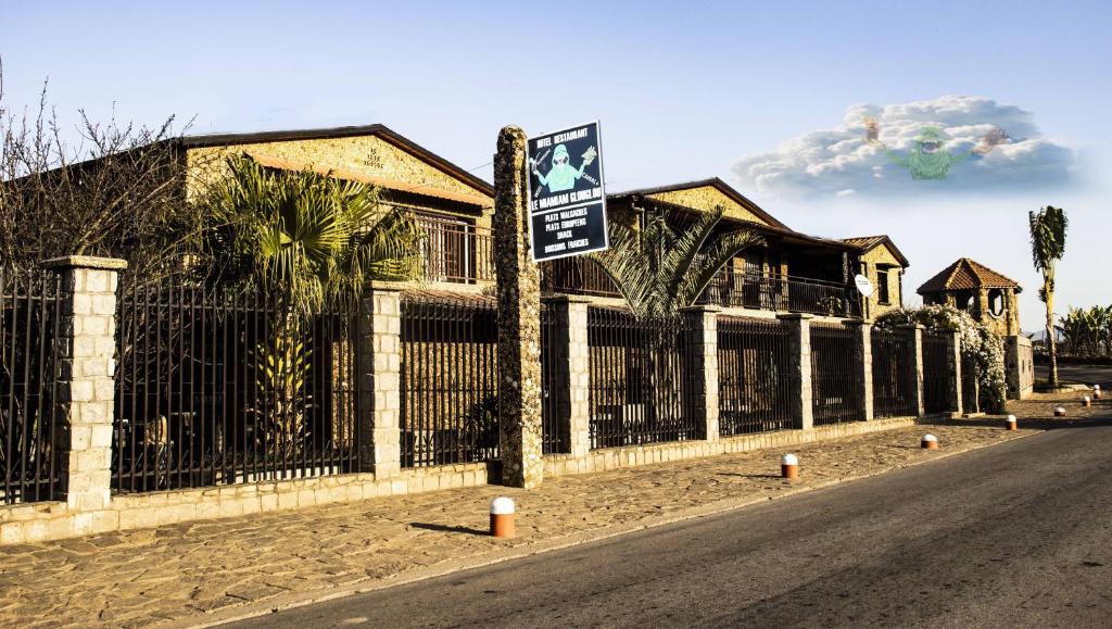ein Haus mit einem Zaun und einem Schild auf einer Straße in der Unterkunft Hôtel restaurant le MIAMIAM GLOUGLOU in Ambositra