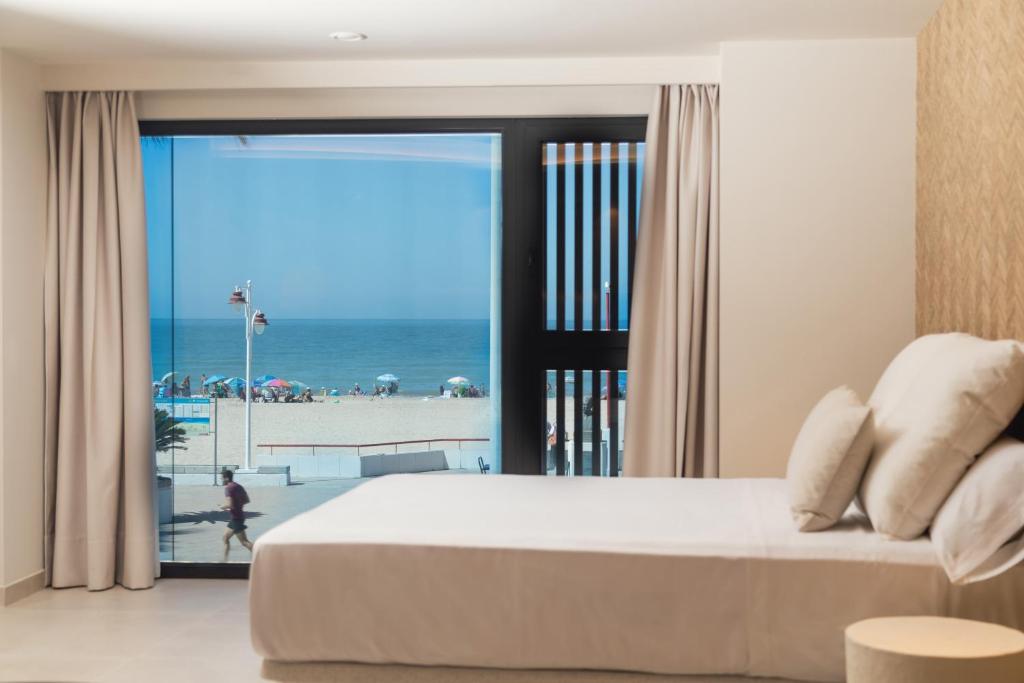 a bedroom with a bed and a view of the beach at Apartamentos Playa Victoria in Cádiz