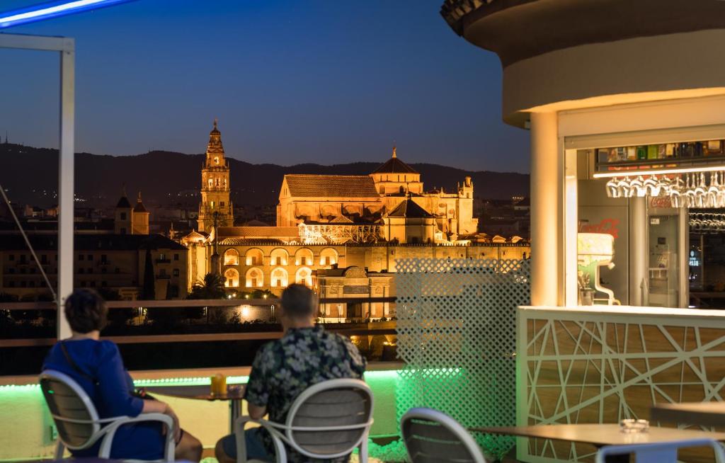 twee personen zitten in stoelen op een balkon met uitzicht op de stad bij Hesperia Córdoba in Córdoba