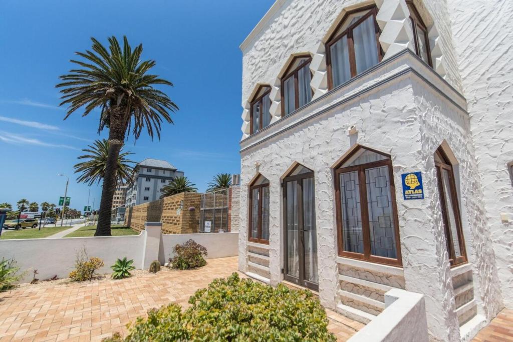 a white house with a palm tree in the background at Villas Marina On The Beach in Port Elizabeth