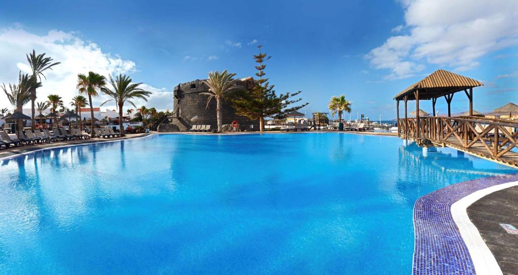 a large blue swimming pool with a gazebo and palm trees at Barceló Fuerteventura Castillo in Caleta De Fuste