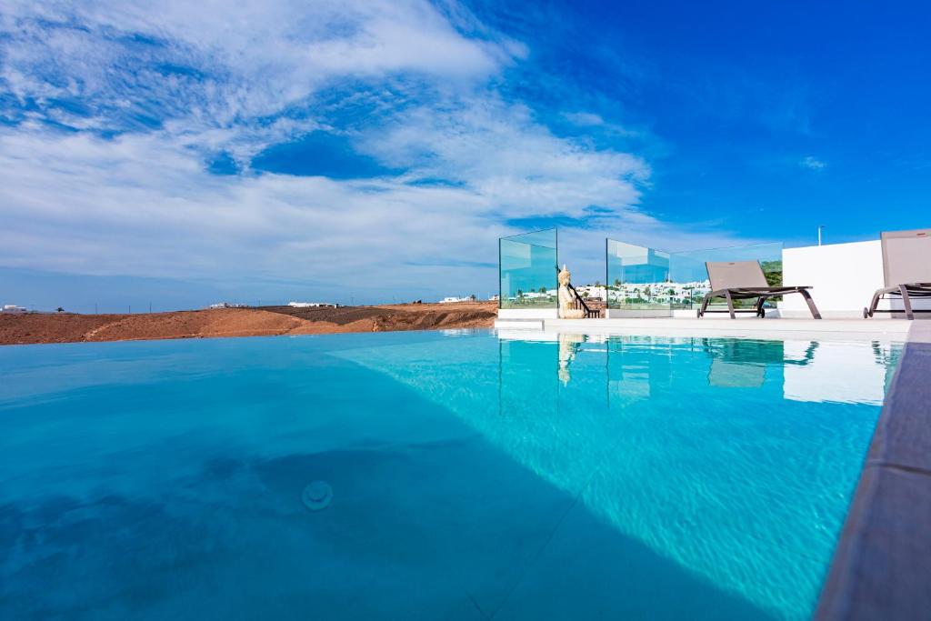 ein Pool mit blauem Wasser und zwei Stühlen in der Unterkunft VILLA PITAYA in Tías