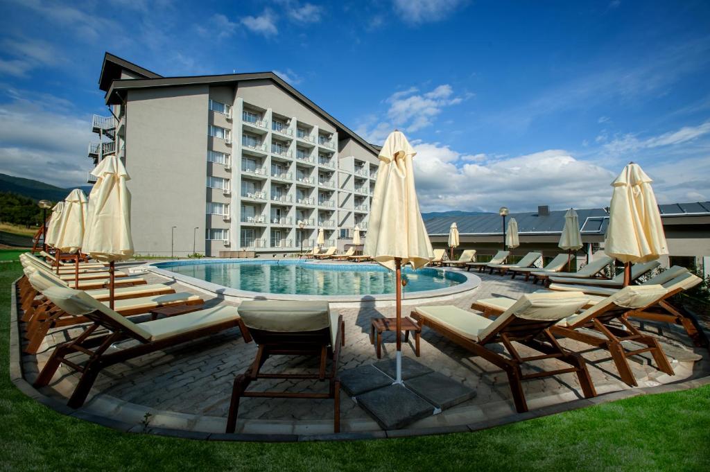 a pool with chairs and umbrellas in front of a hotel at Парк хотел Кюстендил in Kyustendil