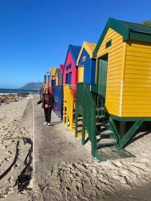 una persona caminando por una playa con casas de playa coloridas en Muizenburg Townhouse- 5 minutes from Surfers Corner en Muizenberg