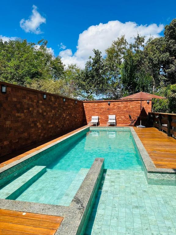 a swimming pool with two chairs and a brick wall at Pousada Império in Serra do Cipo