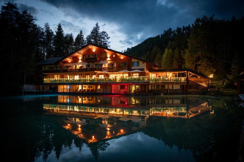 a large building with lights on the water at night at Hotel Lago della Creta in San Vigilio Di Marebbe