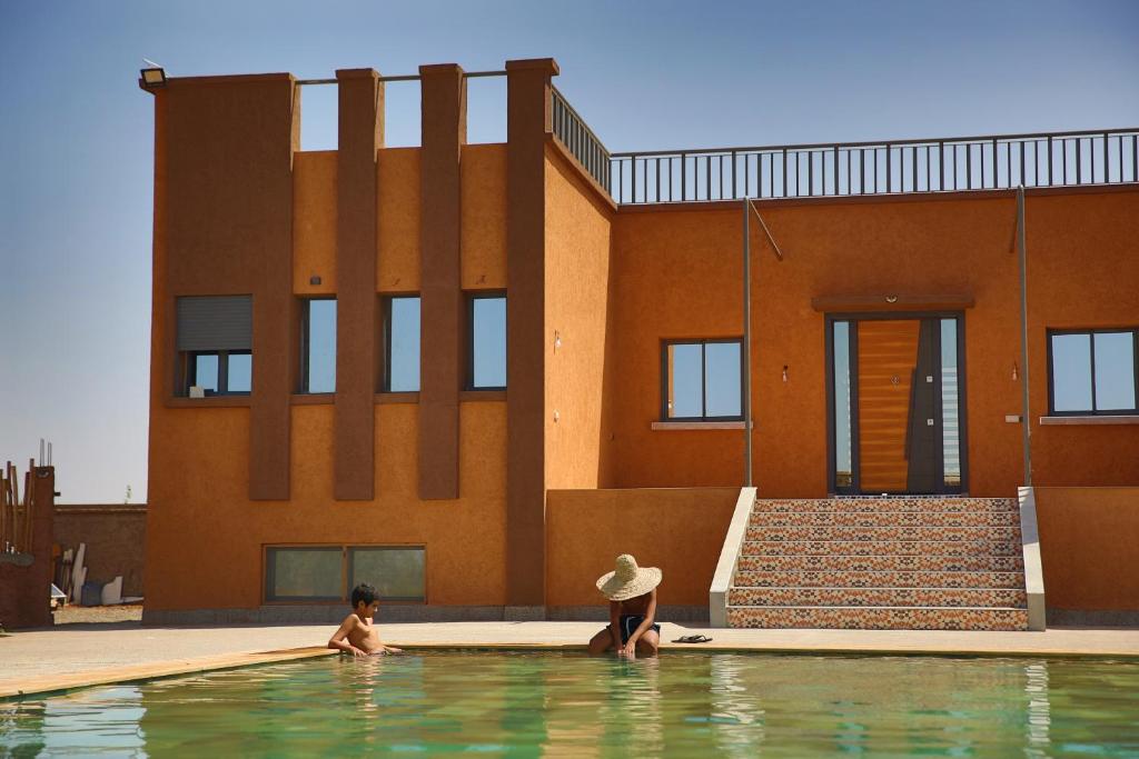 twee personen in een zwembad voor een gebouw bij Dar Koujane Petite maison isolée avec piscine privée 