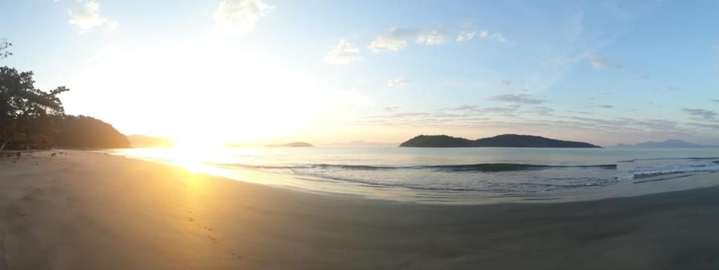 a beach with the sun setting on the water at Casa de 2 andares a 150m da praia! - Prainha de Mambucaba, Paraty - RJ in Paraty