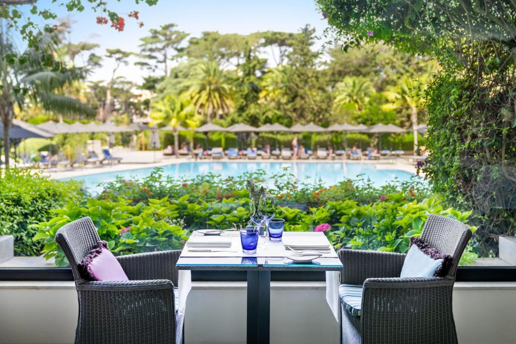 a table with two chairs and a swimming pool at Palácio Estoril Hotel, Golf & Wellness in Cascais
