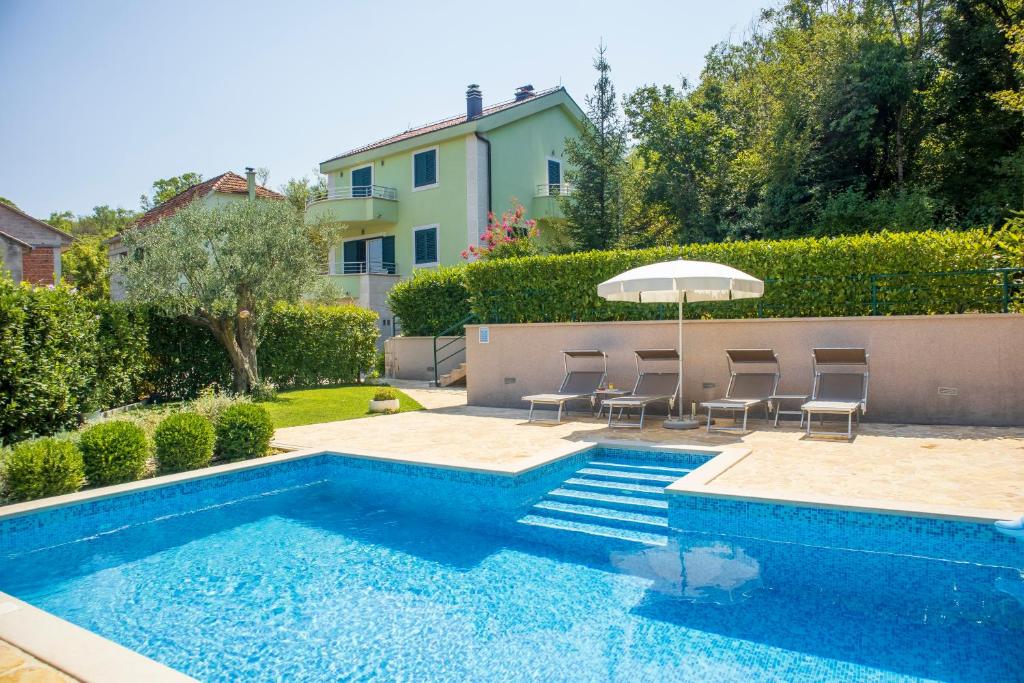 a swimming pool with chairs and an umbrella next to a house at Villa Luna in Imotski