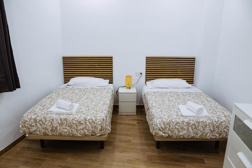 Triana Riverside Guesthouse في إشبيلية: سريرين في غرفة بجدران بيضاء وأرضية خشبية