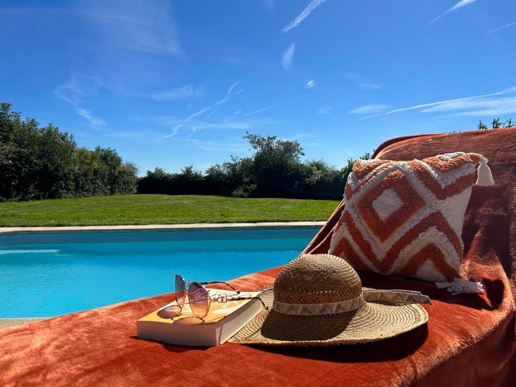 un sombrero y un libro en un sofá junto a una piscina en Le Bain des Hirondelles, en Sprimont