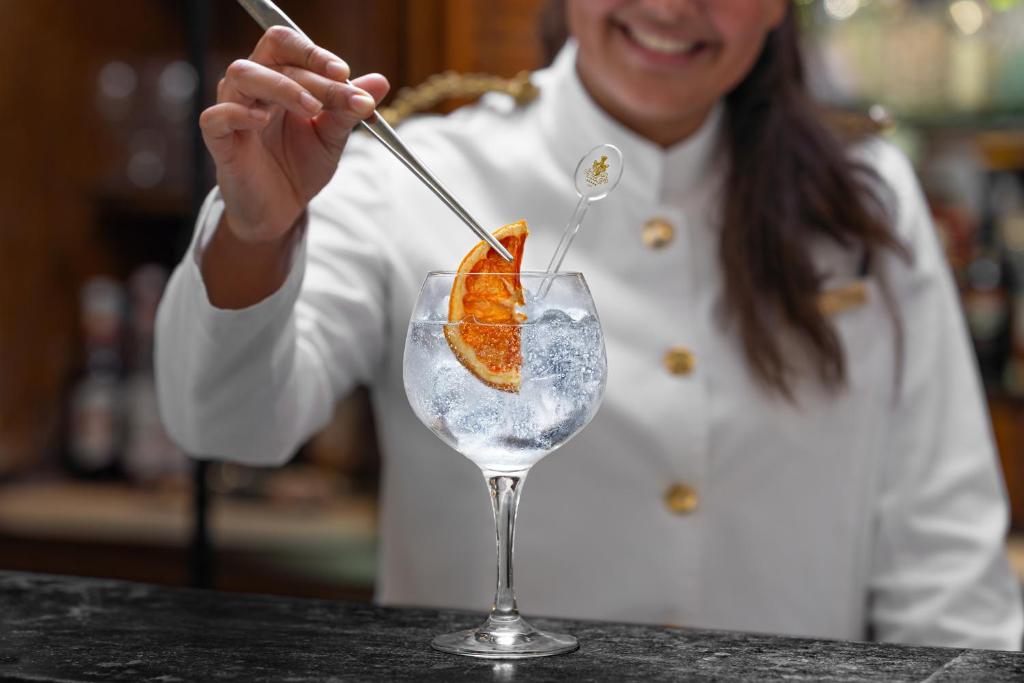 a woman is stirring a glass with an orange in it at Palácio Estoril Hotel, Golf & Wellness in Cascais
