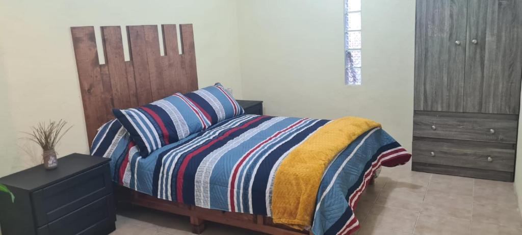 ein Schlafzimmer mit einem Bett mit gestreifter Decke und einer Kommode in der Unterkunft Hospedaje Real Ixiim Habitación (2) personas in Mineral del Monte