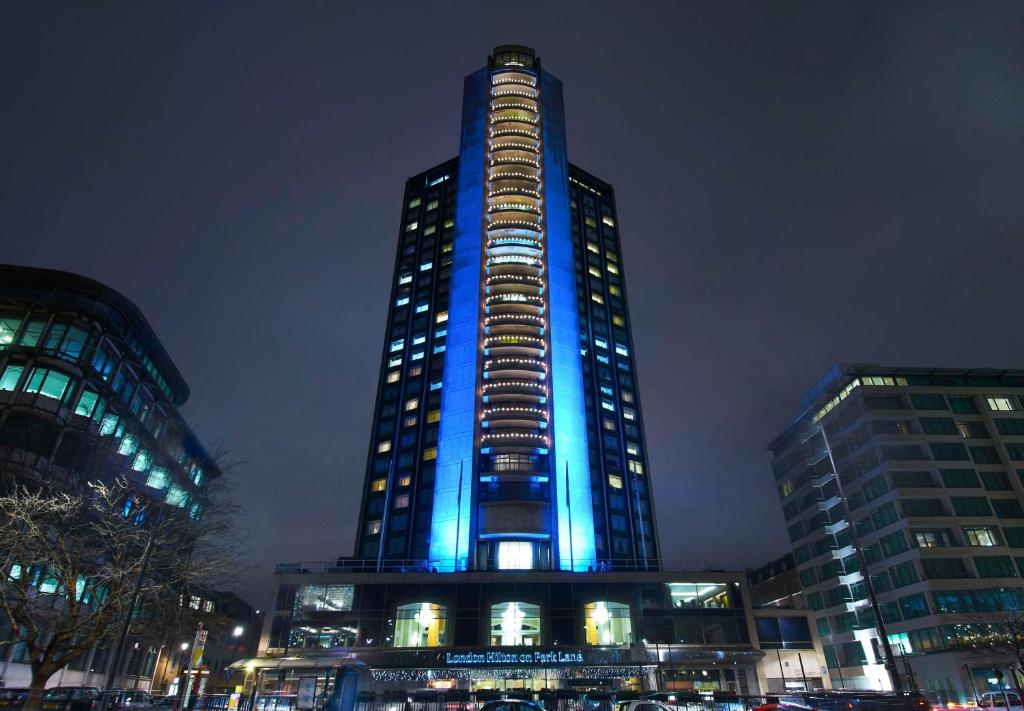 un grand bâtiment avec des lumières bleues allumées la nuit dans l'établissement London Hilton on Park Lane, à Londres