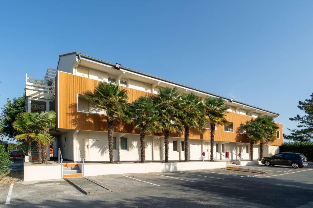 a building with palm trees in a parking lot at Sure Hotel by Best Western Rochefort-sur-Mer in Tonnay-Charente