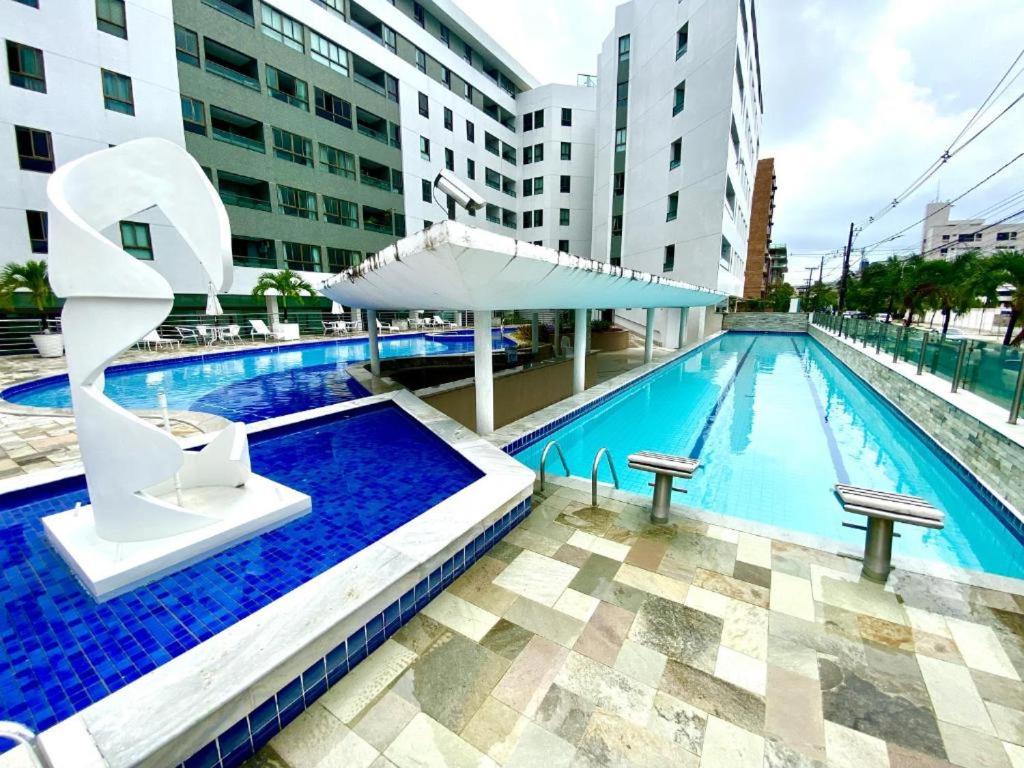 a swimming pool with a white umbrella and some buildings at Loft Luxor Tambaú in João Pessoa