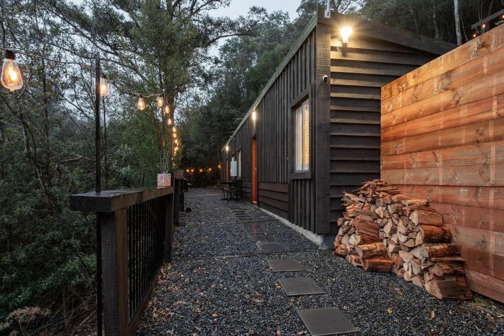 a walkway next to a cabin with a pile of logs at Fernvale Cottage - An Enchanting Mountainside Oasis in Lenah Valley