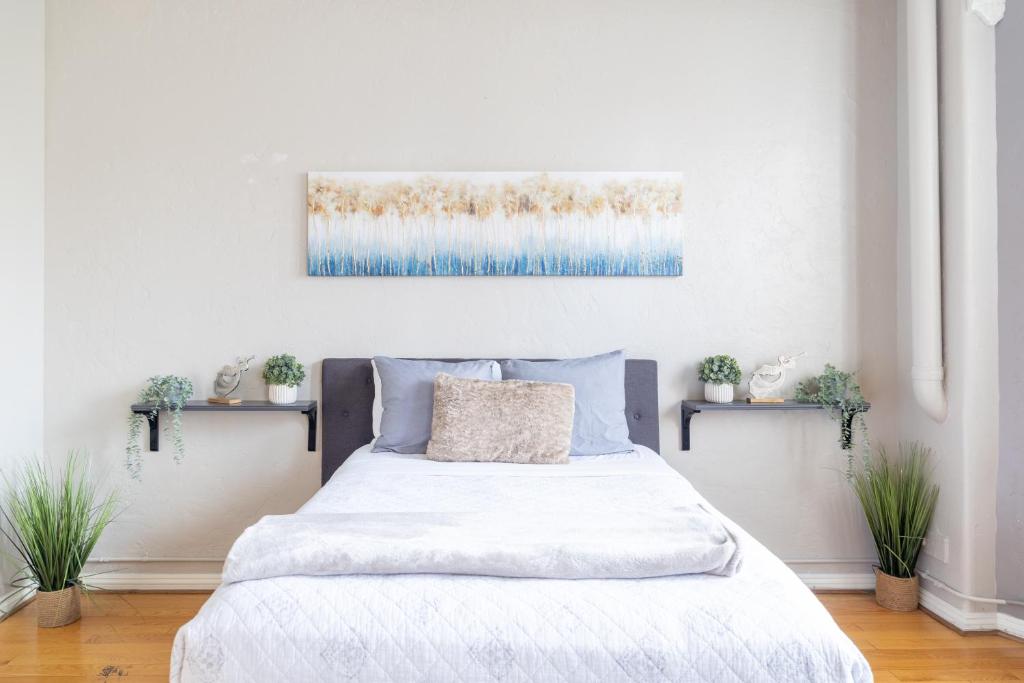 a white bedroom with a bed and two plants at Greely Gaslamp - Loft W Parking & 3 Beds #402 in San Diego