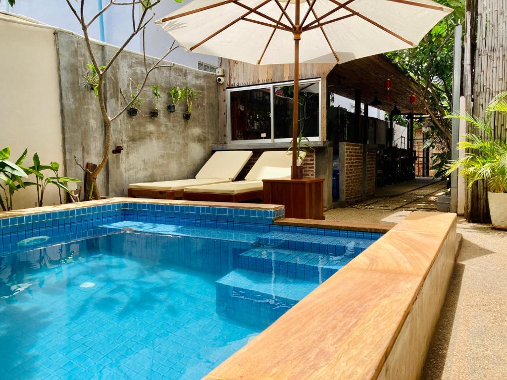 a swimming pool with an umbrella and a bench at Lotus Haven Villa in Siem Reap