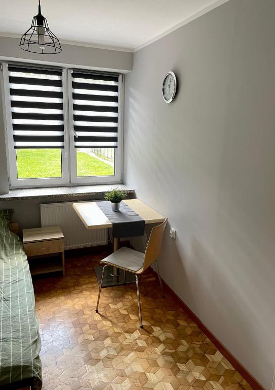a room with a table and a chair and two windows at Kwatery Pracownicze Noclegi Pokoje dla uczniów Kochanowskiego in Wysokie Mazowieckie
