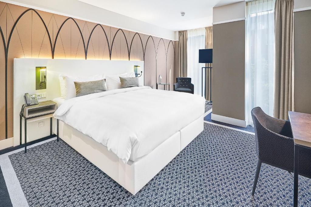 een slaapkamer met een groot wit bed en een bureau bij Hotel Nassau Breda, Autograph Collection in Breda