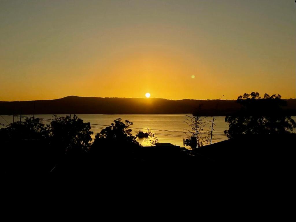 a sunset over a body of water with trees at Spacious 4BR getaway with panoramic water & mountain view in Green Point