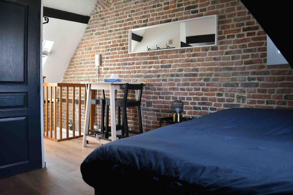 - une chambre avec un mur en briques, un lit et une table dans l'établissement Charmant Studio au Cœur de Béthune, à Béthune