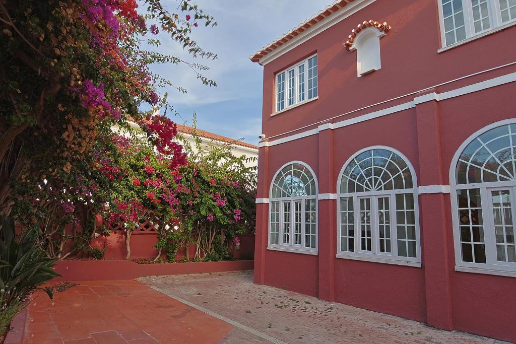 a red building with flowers in front of it at Vila Olivença in Costa da Caparica