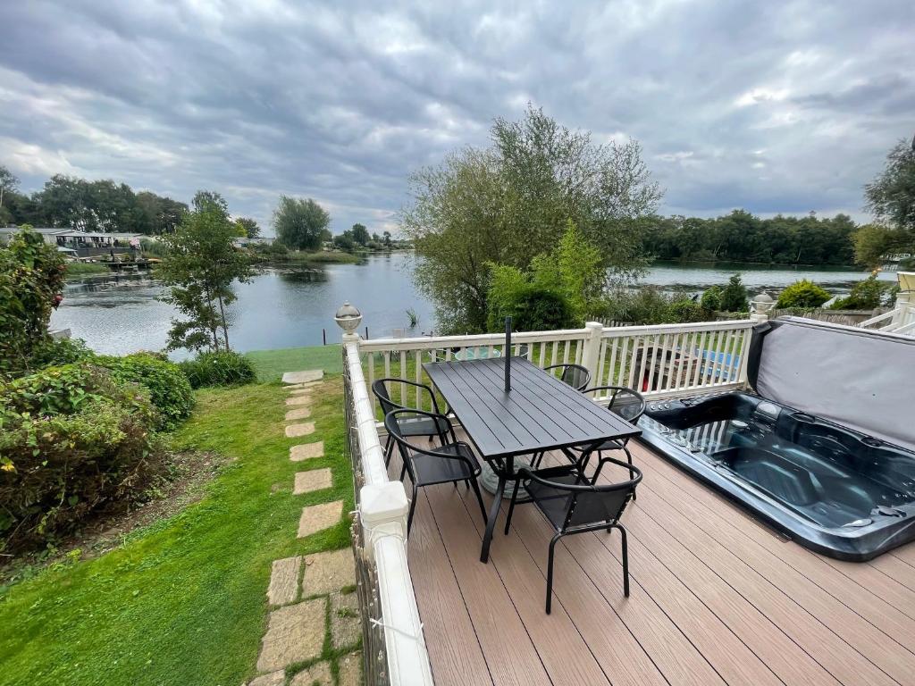 a wooden deck with a table and chairs and a river at Lakeside Retreat 3 with hot tub, private fishing peg situated at Tattershall Lakes Country Park in Tattershall