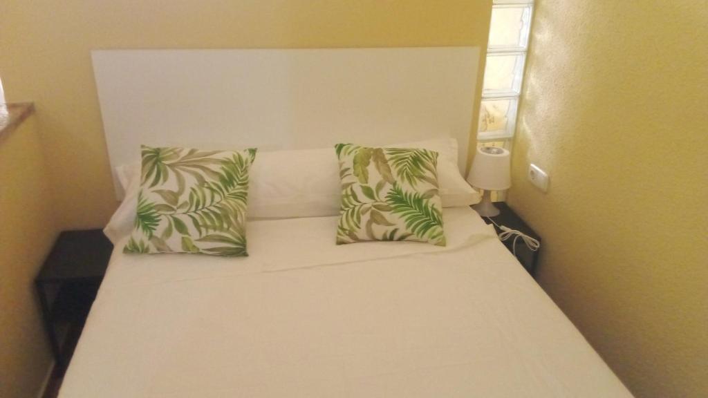 Una cama blanca con dos almohadas verdes. en Sueña Paco, en Torremolinos