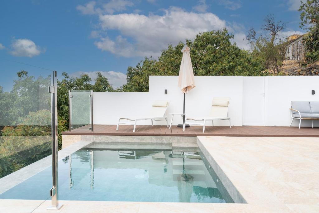 a swimming pool with two chairs and a umbrella on a house at Casa Jade, La Palma in Tijarafe
