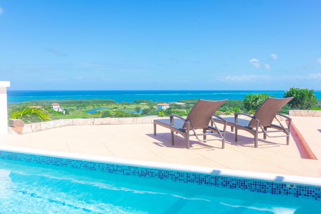 a pool with two chairs and the ocean in the background at Pristine Bay 1303 villa in Roatan