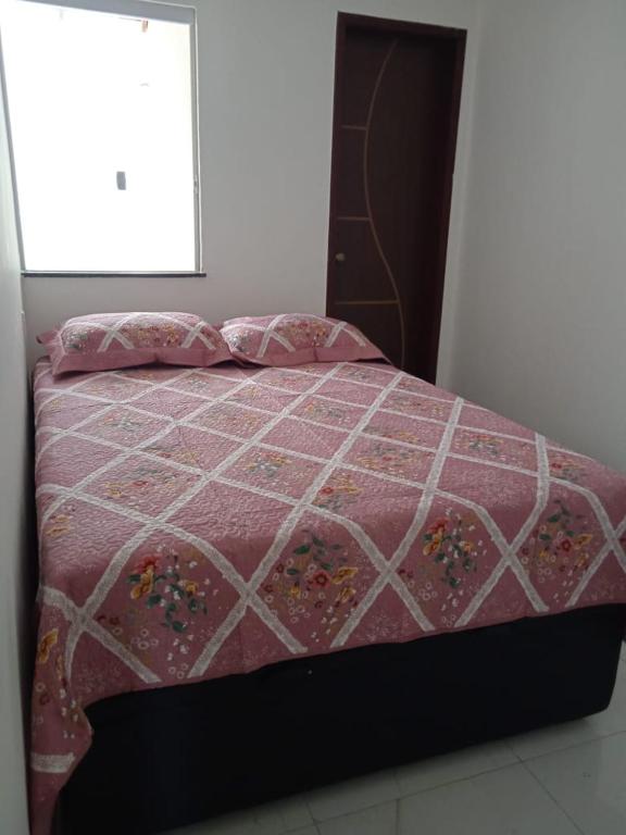 a bed with a pink quilt and a window at Casa em Jauá in Camaçari