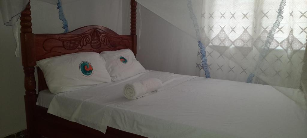 1 cama con cabecero de madera y almohadas blancas en Tranquil Terrace Cottages Diani, en Diani Beach