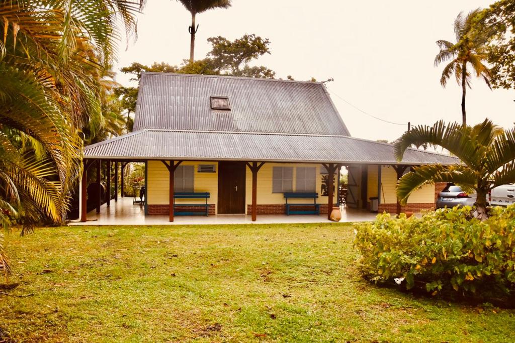 a yellow house with a gray roof and a yard at La villa Gevyrolaine in Gros-Morne