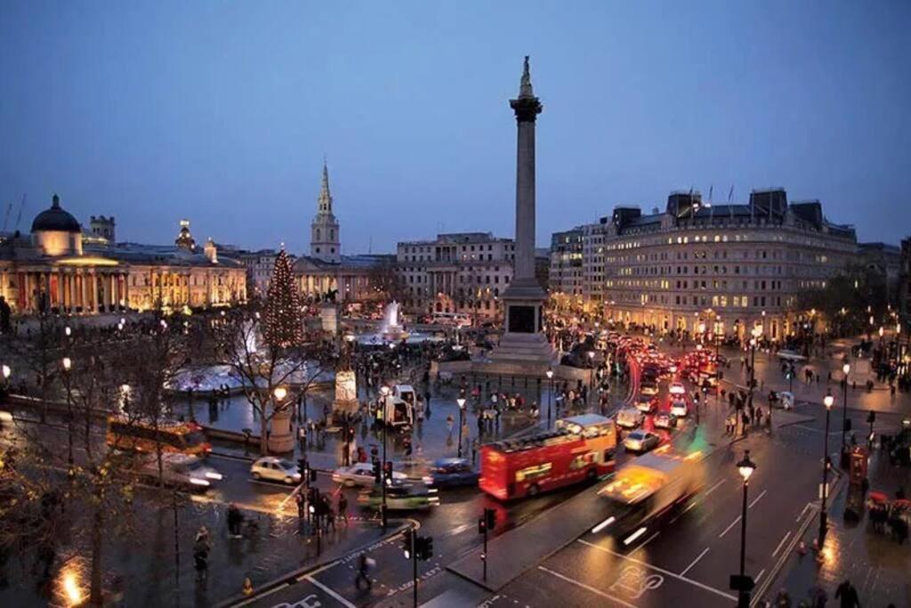 a busy city street with traffic at night with a monument at Trafalgar Square Arty Apartment in London