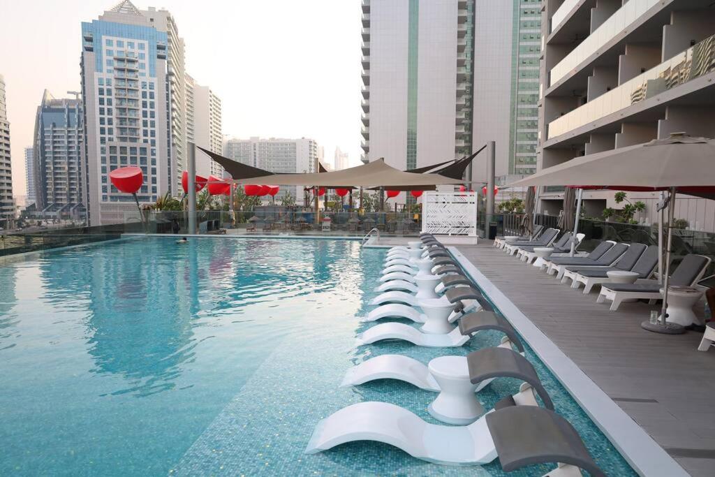 une grande piscine avec des chaises longues et des parasols dans l'établissement MAG 318 DOWNTOWN SUPERIOR ELEGANT STUDIO LAKE VIEW by DOLPHINSUITES, à Dubaï