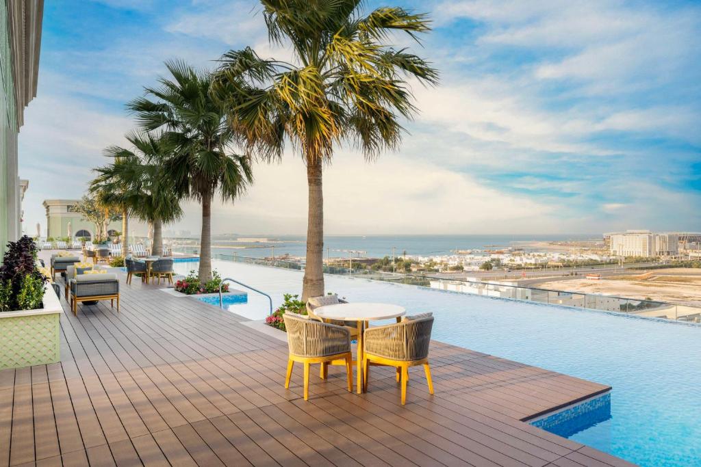 a balcony with a table and chairs and a swimming pool at The Plaza Doha, LXR Hotels & Resorts in Doha